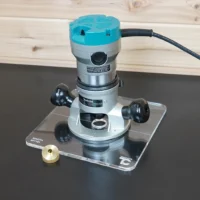 Makita RF1101 router mounted on a 10-inch clear square acrylic guide bushing base plate, with brass bushing nut beside it