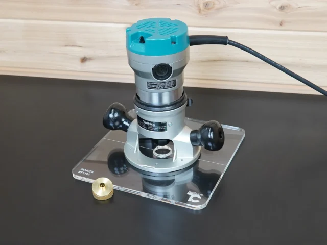 Makita RF1101 router mounted on a 10-inch clear square acrylic guide bushing base plate, with brass bushing nut beside it
