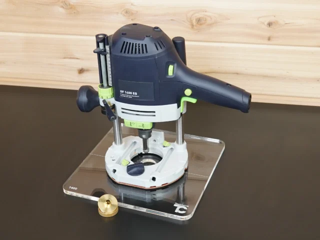 Festool OF 1400 router mounted on a clear 10-inch square acrylic guide bushing base plate, brass nut beside it