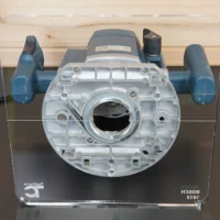 Clear acrylic square base plate mounted on Bosch 1613 router from above, showing central opening and mounting holes