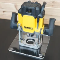 DeWalt 625 plunge router mounted on a clear acrylic square base plate, shown from front angle on a display stand