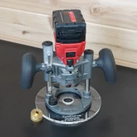 8-inch clear acrylic round router base plate mounted on a Milwaukee M18 trim plunge router, with brass guide bushing alongside