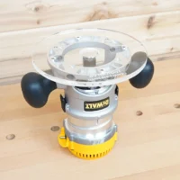 8-inch clear acrylic router base plate mounted on a Dewalt DW618 plunge router, showing top view with guide bushing opening and black knobs on yellow motor housing