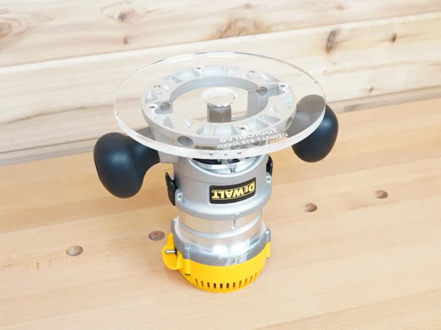 8-inch clear acrylic router base plate mounted on a Dewalt DW618 plunge router, showing top view with guide bushing opening and black knobs on yellow motor housing