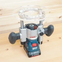 Clear 8-inch round acrylic router base plate mounted on an inverted Bosch Colt plunge router base, center bushing opening visible