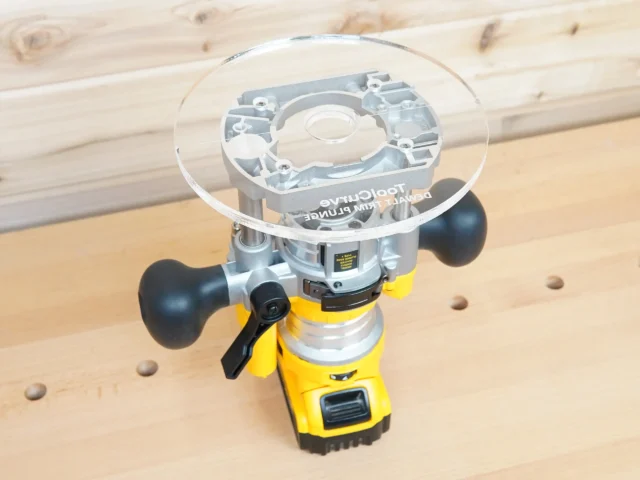 Clear 8-inch round acrylic router base plate marked Dewalt Trim Plunge, mounted on a yellow Dewalt DNP612 plunge router