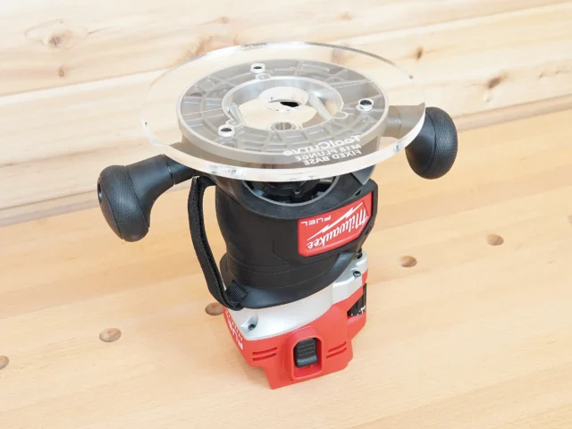 Clear 8-inch round acrylic router base plate mounted upside down on a Milwaukee M18 Fuel router
