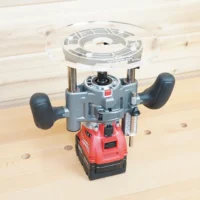 Clear 8-inch round acrylic router base plate mounted upside down on a Milwaukee M18 trim plunge router