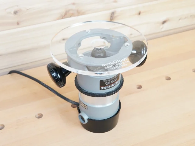 8-inch clear acrylic router base plate mounted on a Porter Cable 690 series router, showing the transparent top with internal mounting mechanism and black adjustment knob on the side.