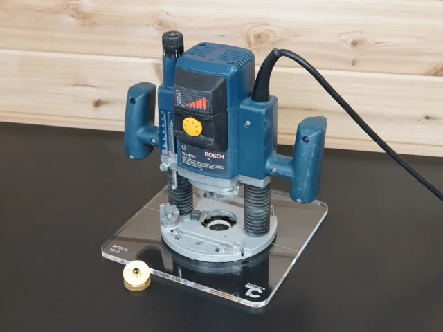 Bosch 1613EVS plunge router mounted on a 10" clear acrylic guide bushing base plate, with brass ring alongside