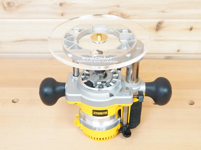 Clear acrylic 8-inch router base plate mounted on yellow Dewalt DW618 plunge router, viewed from above showing brass center insert and mounting hardware