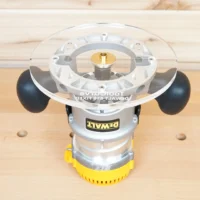 8-inch clear acrylic router base plate mounted on a Dewalt DW618 plunge router, showing the transparent top surface with brass center bushing and black knob handles on either side