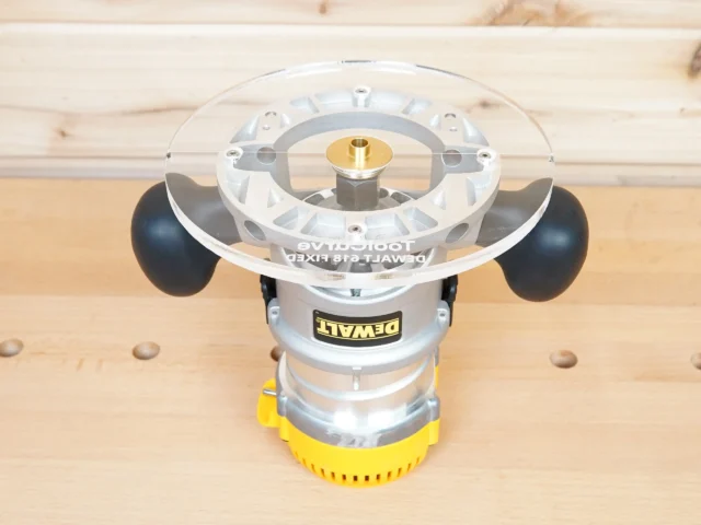 8-inch clear acrylic router base plate mounted on a Dewalt DW618 plunge router, showing the transparent top surface with brass center bushing and black knob handles on either side