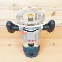Clear acrylic router base plate with 8-inch diameter mounted on a Bosch MR23EVS plunge router, showing brass center insert and black grip handles
