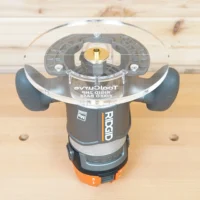 8-inch clear acrylic router base plate mounted on a Ridgid 2 HP fixed base router, viewed from above on a wood workbench