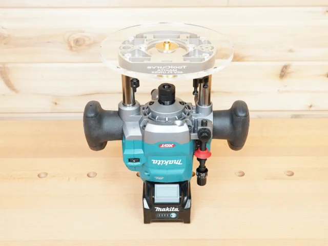 8-inch clear acrylic router base plate mounted on a Makita 40v cordless router, shown from above on a wooden workbench