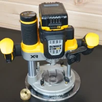 8-inch round clear acrylic guide bushing base plate mounted on a DeWalt 20V XR plunge router, brass bushing beside it