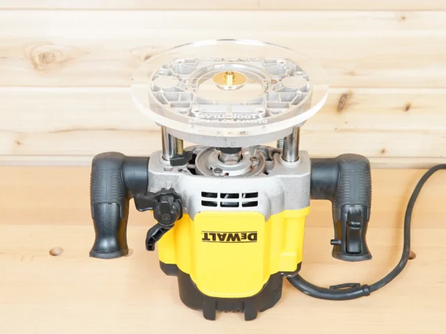 DeWalt plunge router with yellow housing and black handles, fitted with clear acrylic 8-inch round base plate, viewed from above on wooden workbench