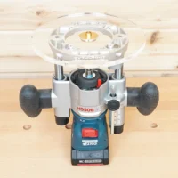 8-inch clear acrylic router base plate mounted on a Bosch plunge router, top and front view on wood workbench
