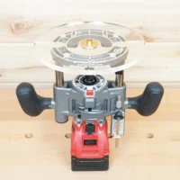 8-inch clear acrylic router base plate mounted on red Milwaukee M18 trim plunge router, shown from above on wooden workbench