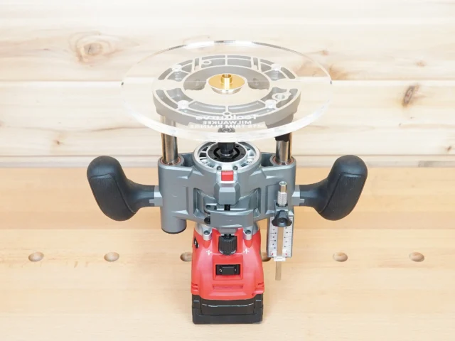 8-inch clear acrylic router base plate mounted on red Milwaukee M18 trim plunge router, shown from above on wooden workbench