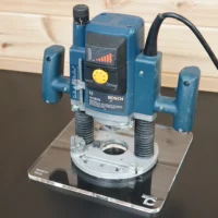10-inch square clear acrylic base plate attached to a Bosch 1613 plunge router, viewed from above on a work surface