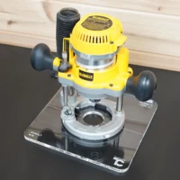 10-inch clear acrylic square base plate installed on a yellow DeWalt DW618 plunge router, mounted on a clear acrylic display platform