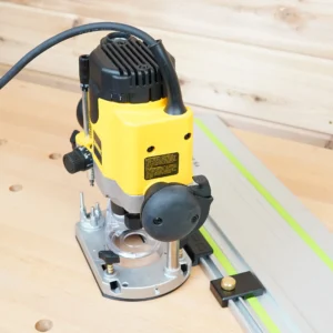 Yellow Dewalt DWE621 plunge router mounted on a guide rail adapter riding a track on a wood bench