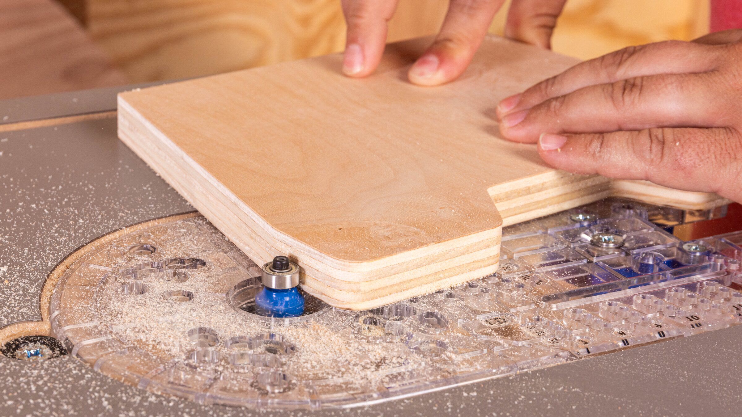 A plywood workpiece being guided past a bearing-guided bit in the clear Dock & Go baseplate
